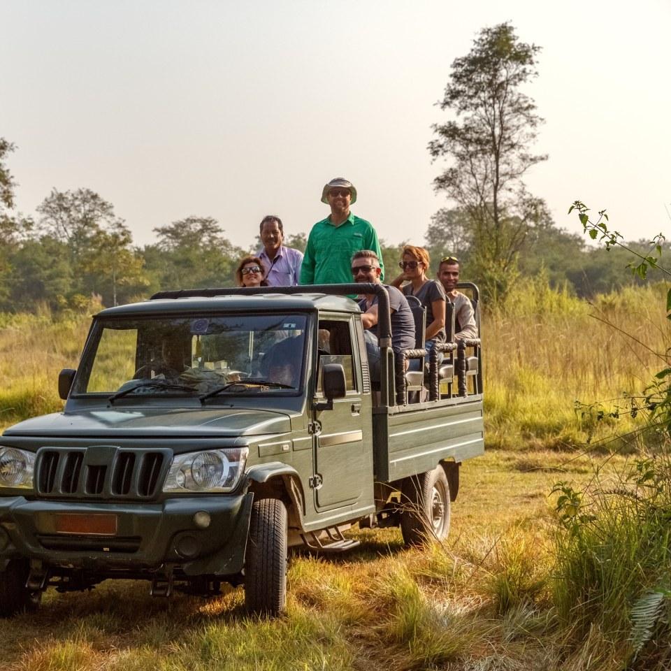 A wildlife photographer or traveller observing a one-horned rhinoceros in the grasslands of Chitwan.